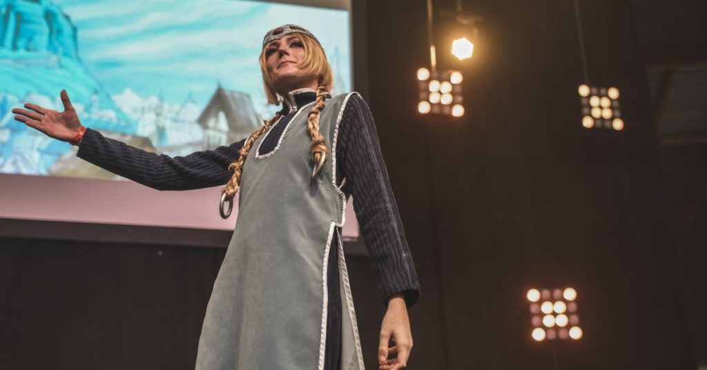 Défilé cosplay sur scène au festival Geek Life, participante en costume médiéval devant un décor animé