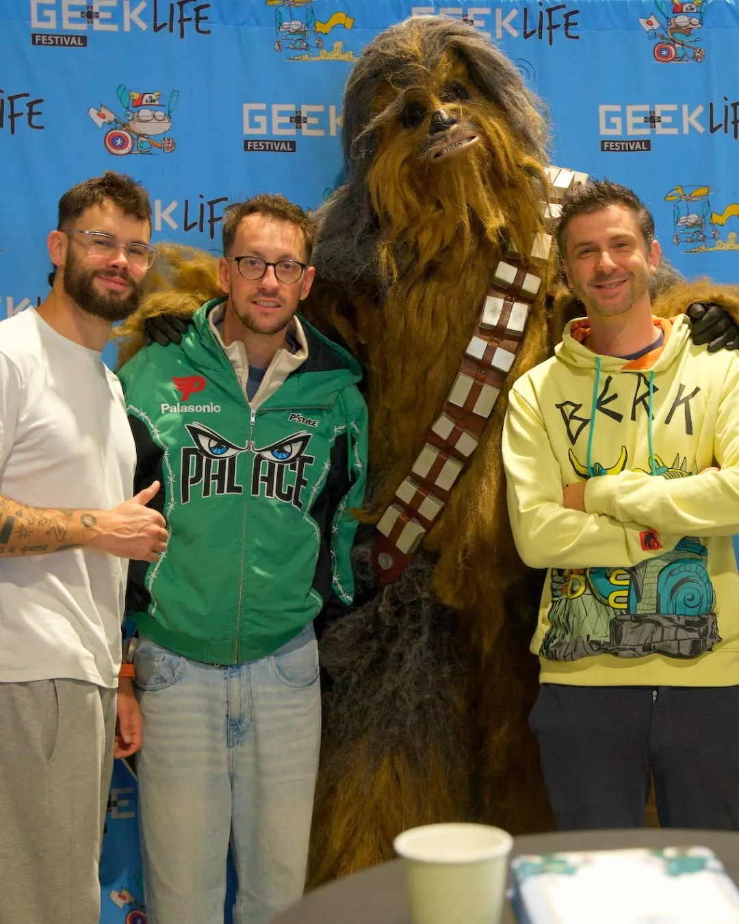 Des invités de Geek Life posent avec Chewbacca devant le mur du festival